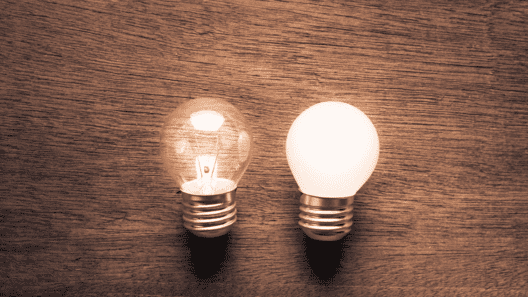 木目調の背景。真ん中には2つの電球。左の電球は消えていて、右の電球は点灯している画像。